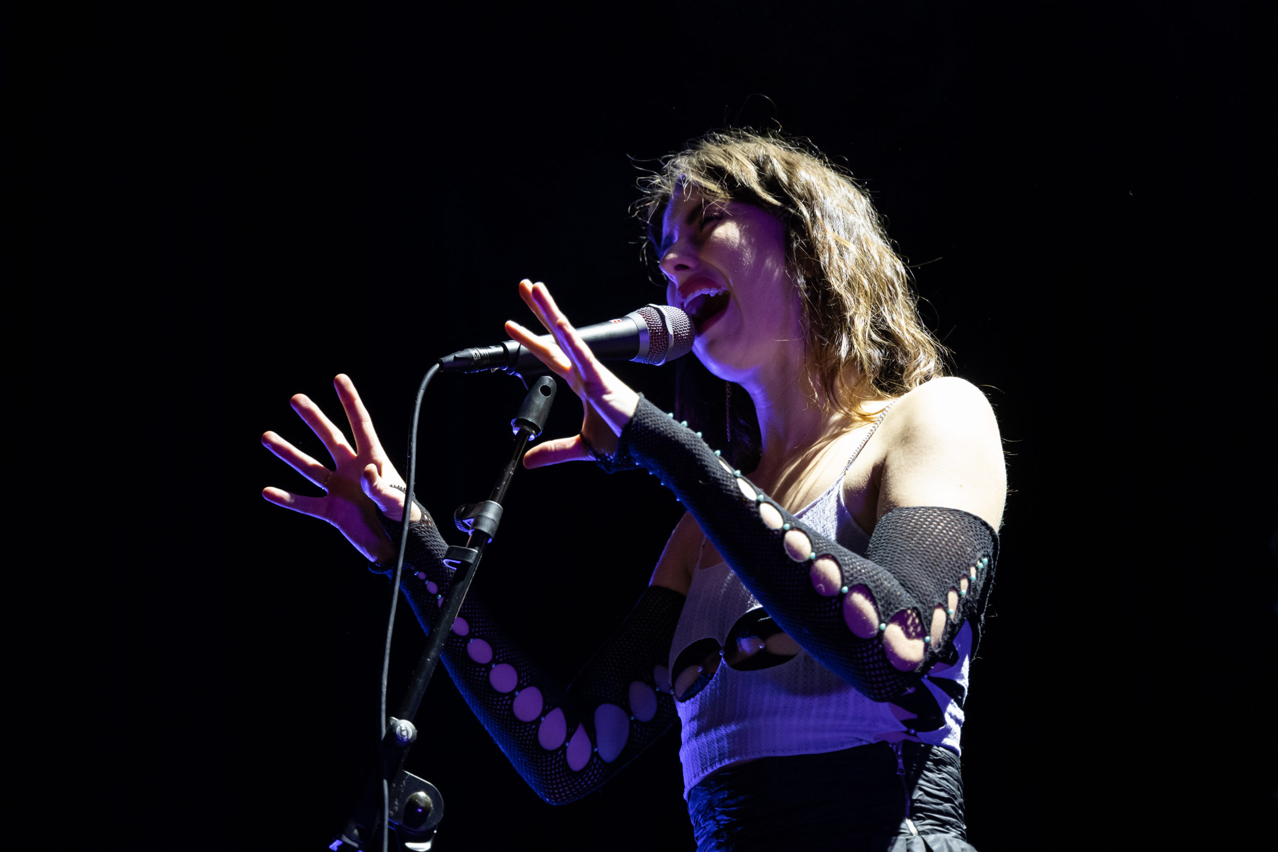 Kimbra sings dramatically into a microphone her hands up in front of her.