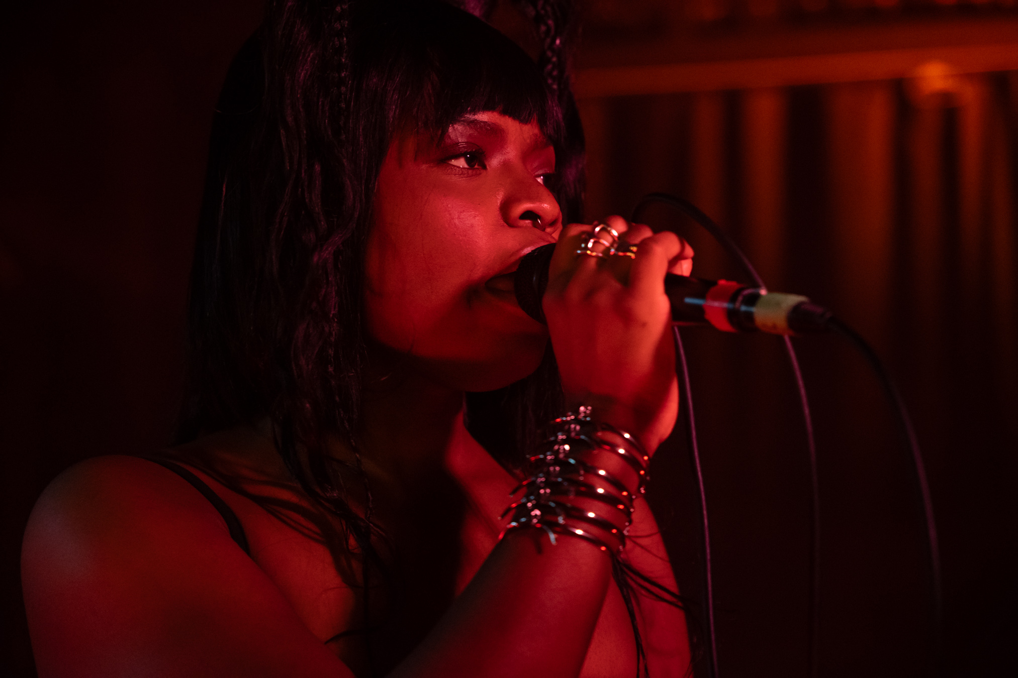 Vagabon holds the microphone in her hand with an arm covered in bracelets, singing at the Biltmore Cabaret