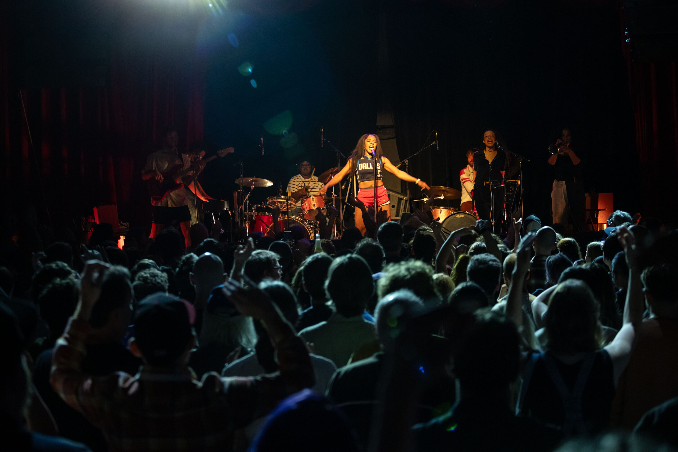 The Go! Team are on the stage at The Pearl with the audience lit up in blue light and a lens flare