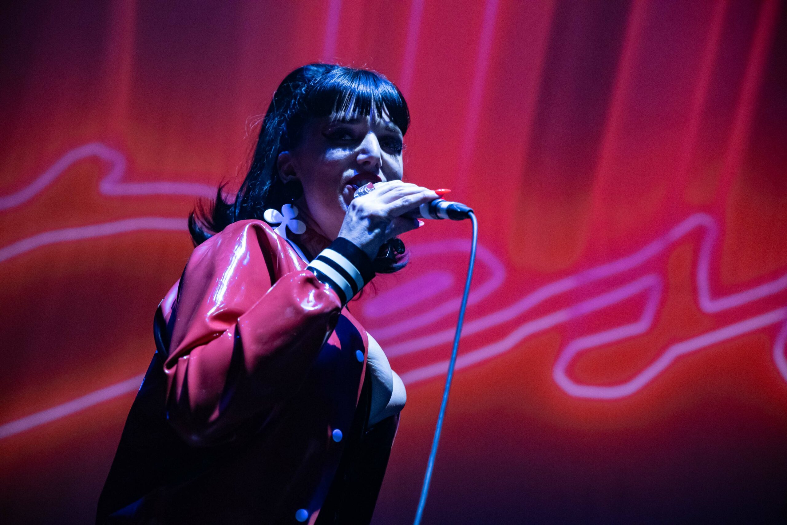 The singer from Desire sings into a microphone with their band's logo projected behind her