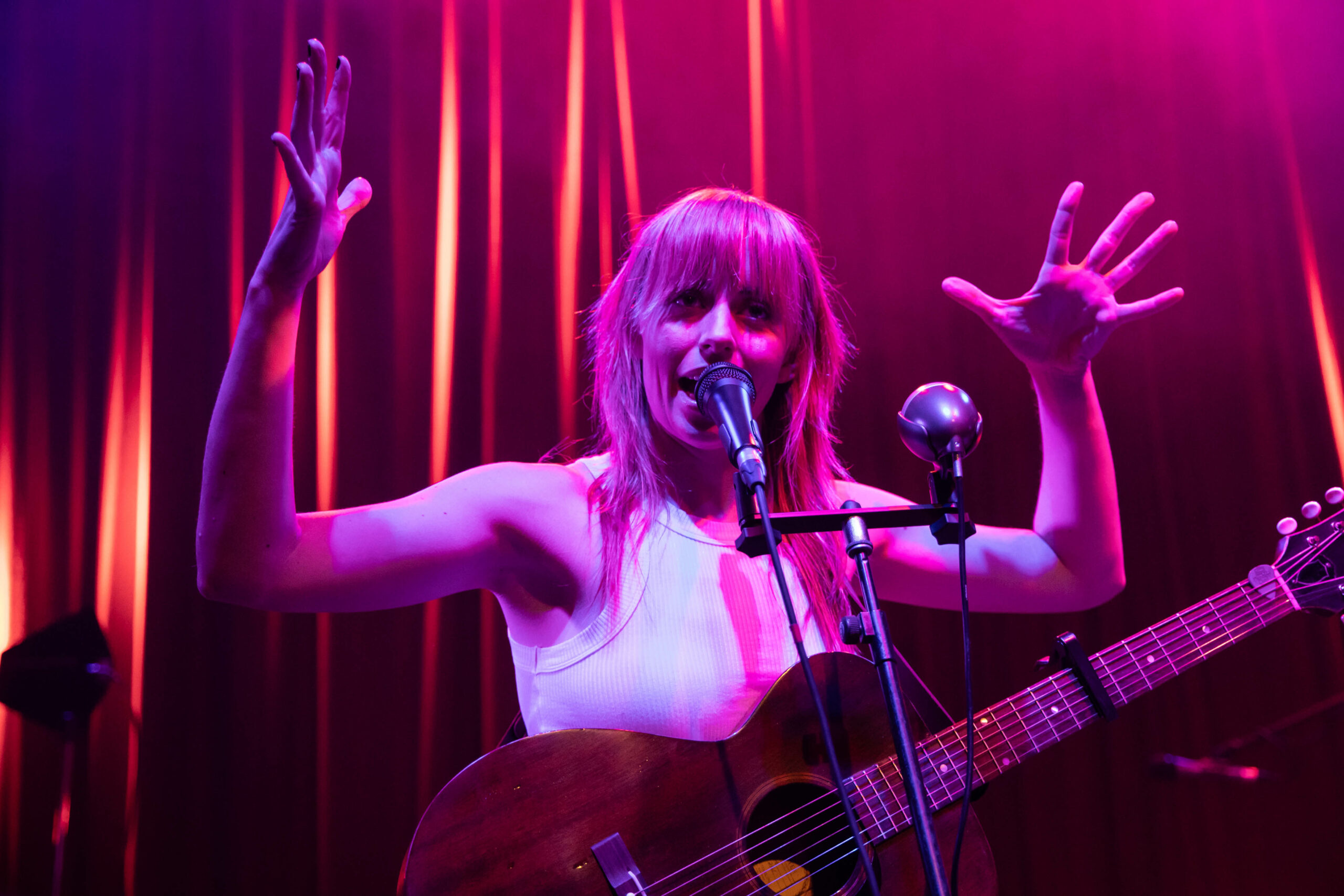 Gordi gestures with both hands with an acoustic guitar around her neck at the Fox Cabaret in Vancouver