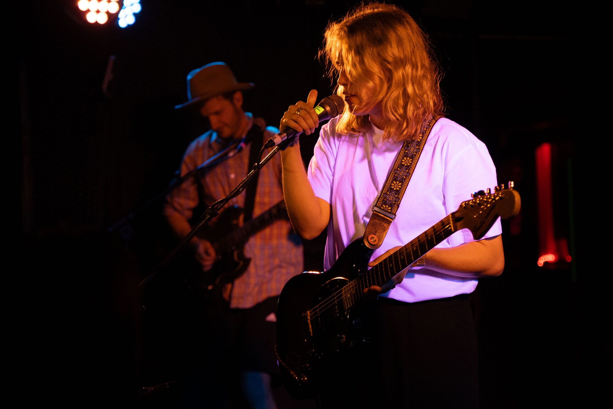 Marika Hackman sings into and holds the microphone on the stage in purple and orange light.