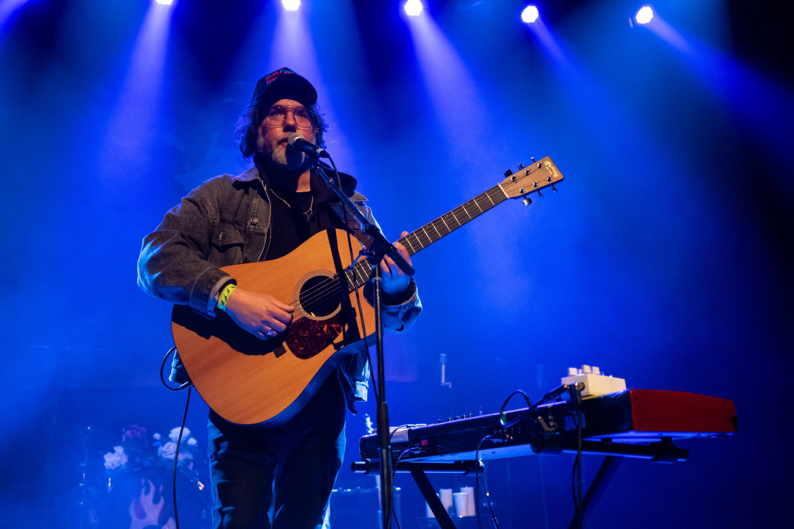 Kevin Drew is on the stage of the Vogue Theatre backlit in blue light