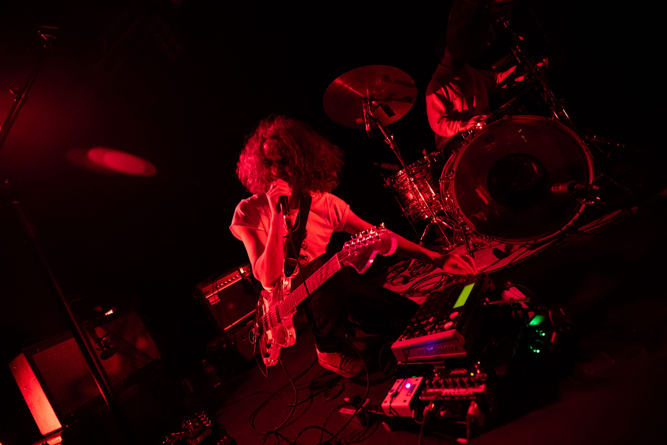 The frontman from Suuns crouches by his effects rack while singing into the microphone